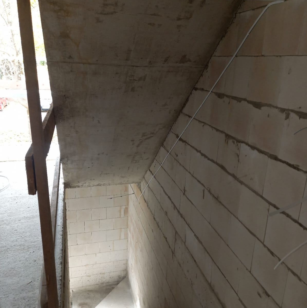 Wewnętrzne ściany z białych bloczków, surowy betonowy strop i biały przewód elektryczny prowadzony po ścianie, widok z dołu w trakcie budowy.