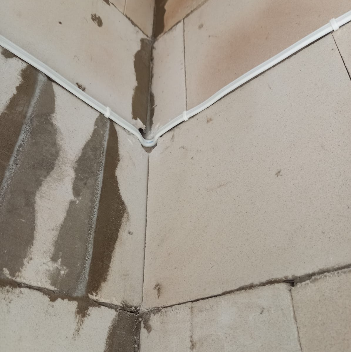 Biała listwa kablowa przymocowana do surowych ścian z betonu komórkowego w rogu pomieszczenia, widoczne ślady po zaprawie.
