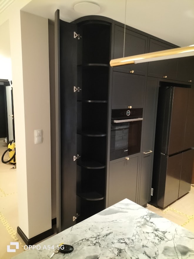 Ciemna zabudowa kuchenna z otwartą szafką narożną z półkami, widoczny fragment blatu z marmuru i sprzęt AGD.