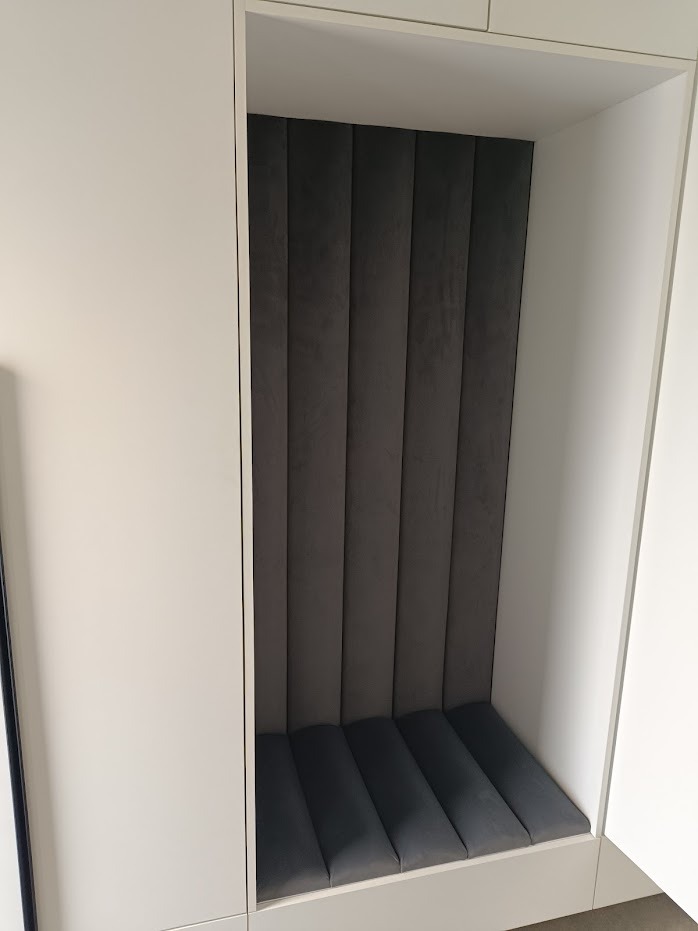 Wnęka z tapicerowanym siedziskiem i panelem ściennym w odcieniach szarości, wbudowana w białą szafę.