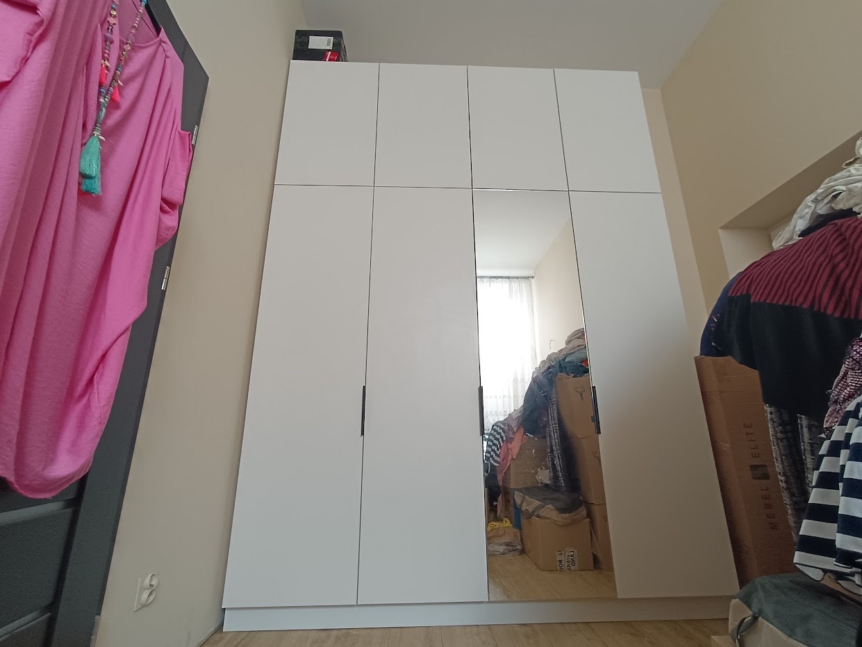 Biała szafa wnękowa z lustrzanymi drzwiami w mieszkaniu w Rembertowie, widoczny bałagan odbijający się w lustrze.
