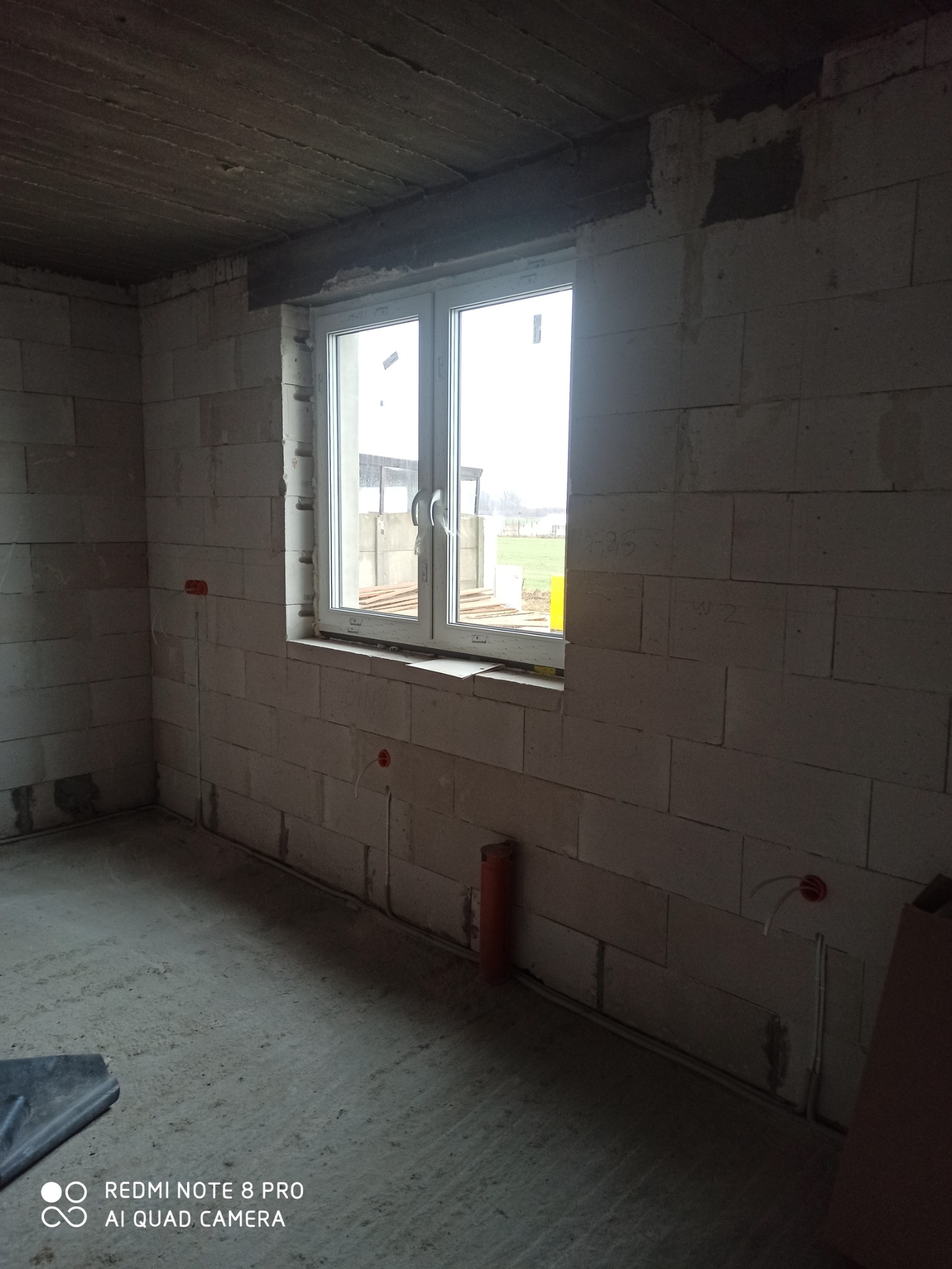 Surowy stan wnętrza z oknem, widoczne wyprowadzone przewody elektryczne w ścianie z bloczków.
