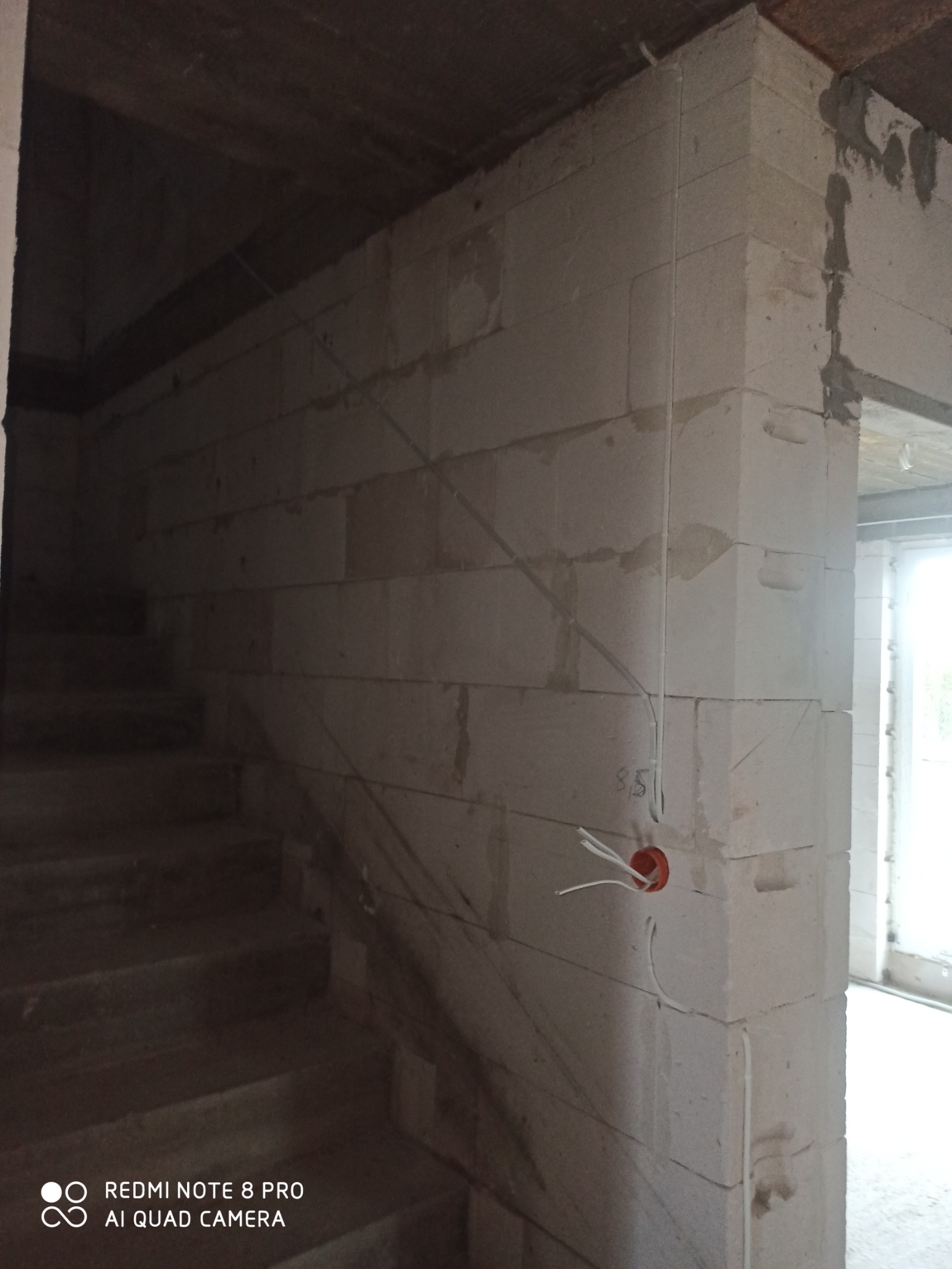 Wewnętrzne ściany z betonu komórkowego w trakcie budowy, widoczne przewody elektryczne wystające z puszki instalacyjnej, obok schody.