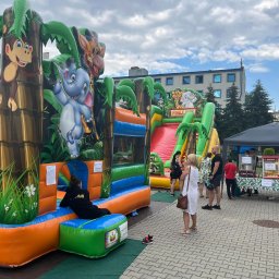 Playlandoo Michał Skowron - Dwa dmuchane zamki w stylu dżungli z motywami zwierzęcymi, ustawione na zewnątrz podczas imprezy plenerowej, z osobami w tle i stoiskiem z watą cukrową widocznym po prawej stronie.