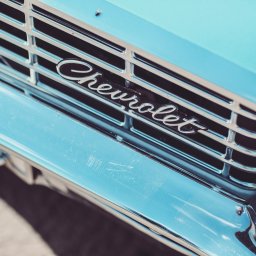 Fotorama24 - Chromowana atrapa chłodnicy z napisem 'Chevrolet' na turkusowym samochodzie, widoczne drobne zarysowania na lakierze.