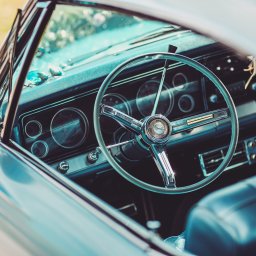 Fotorama24 - Wnętrze klasycznego samochodu z chromowaną kierownicą i deską rozdzielczą, widoczne okulary przeciwsłoneczne na desce.