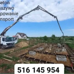 Betonomieszarka z wysięgnikiem pompuje beton do szalunków fundamentowych na placu budowy domu jednorodzinnego z widocznym w tle domem.