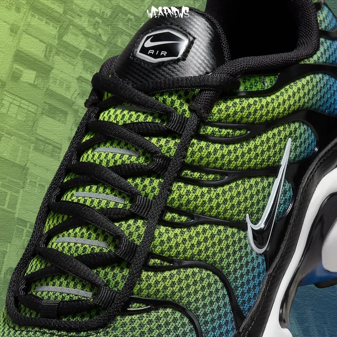 Zbliżenie na fragment sportowego buta z siateczkową teksturą w odcieniach zieleni i błękitu, czarne sznurowadła i logo producenta na języku, na rozmytym tle budynki.