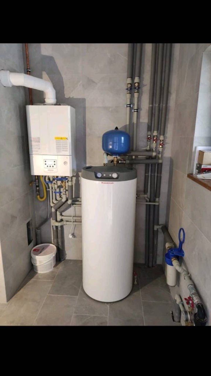 Nowoczesna kotłownia z białym piecem gazowym kondensacyjnym i zasobnikiem ciepłej wody, rury w kolorze szarym, estetyczne wykończenie w szarościach.