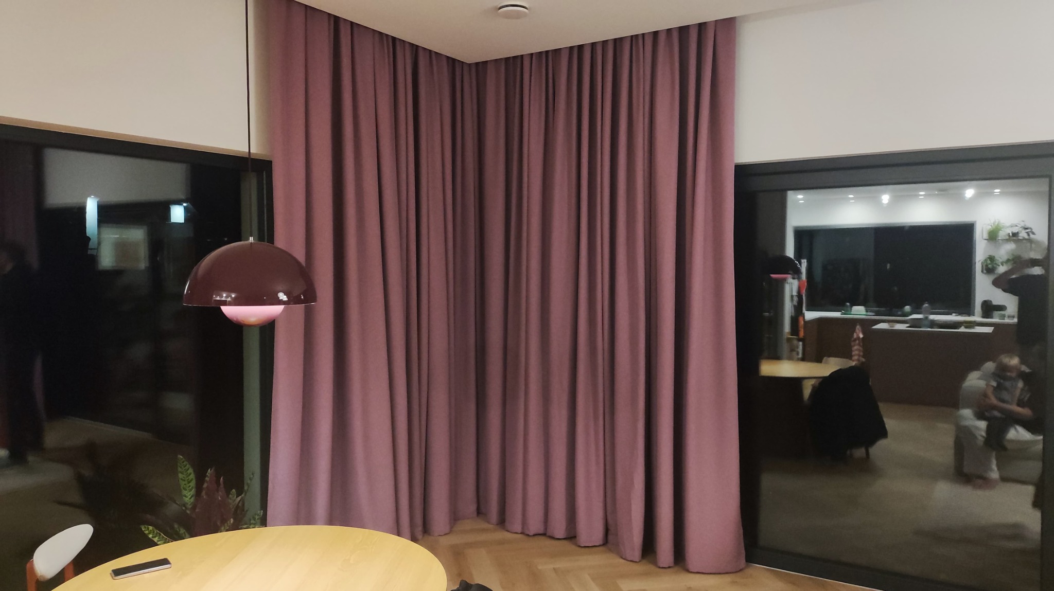 Zasłony w odcieniach różu, wiszące od sufitu do podłogi, tworzą przytulną atmosferę w nowoczesnym wnętrzu. Widoczne fragmenty stołu i lampy.
