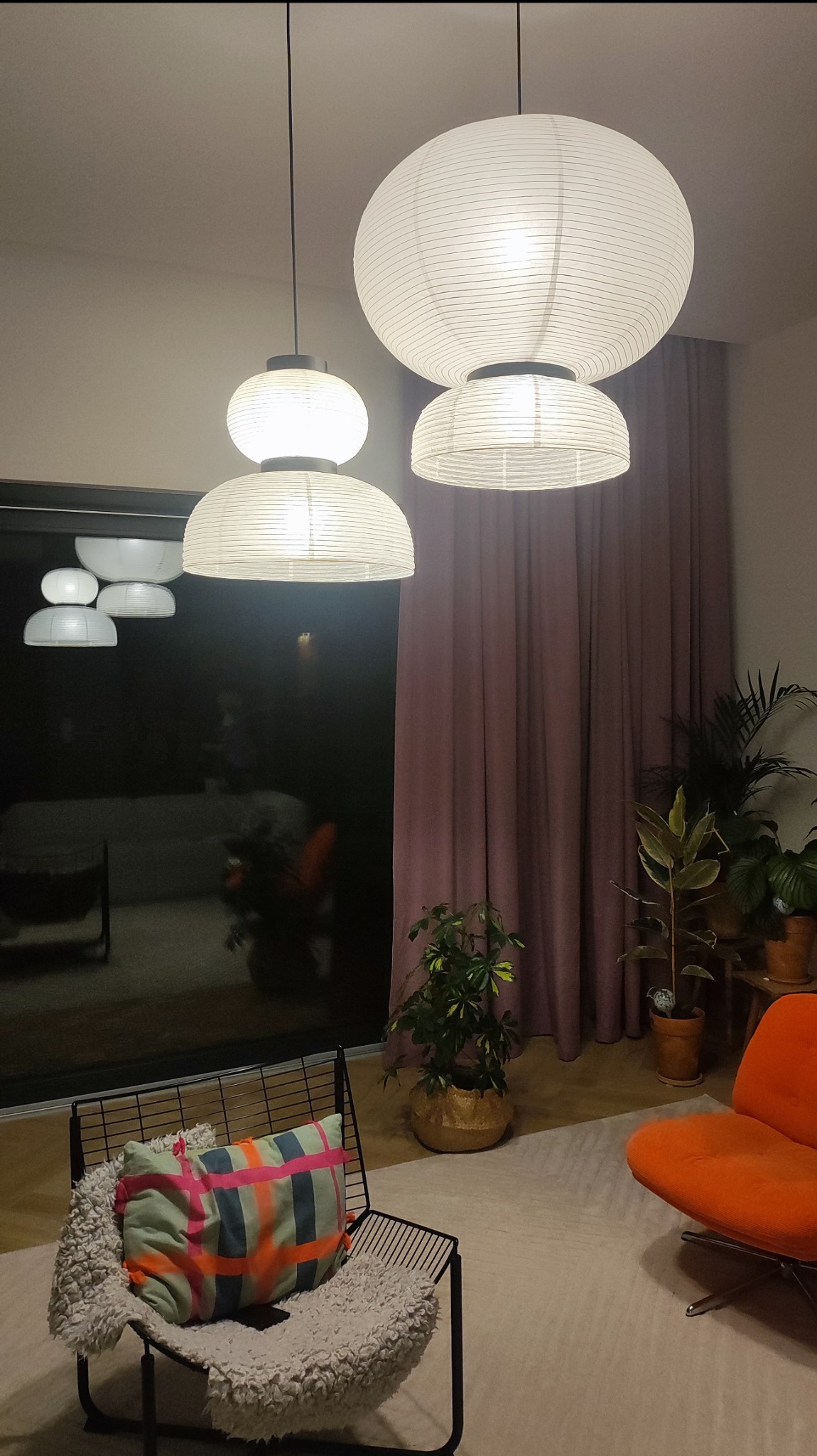 Nowoczesne wnętrze z trzema papierowymi lampami wiszącymi o różnej wielkości, oświetlającymi pokój z zasłonami i roślinami doniczkowymi.