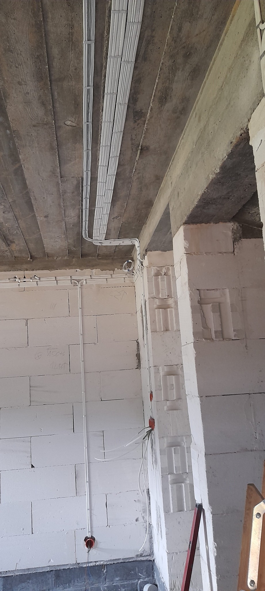 Kable elektryczne prowadzone po suficie i ścianach w surowym wnętrzu budynku z bloczków, widoczne puszki instalacyjne i przewody.