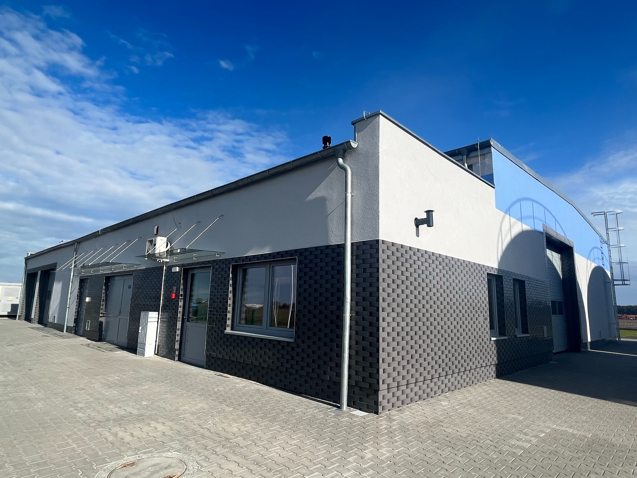 Nowoczesny budynek Stacji Uzdatniania Wody z elewacją w odcieniach szarości, wykończony cegłą klinkierową i jasnym tynkiem, widoczny z zewnątrz przy słonecznej pogodzie.