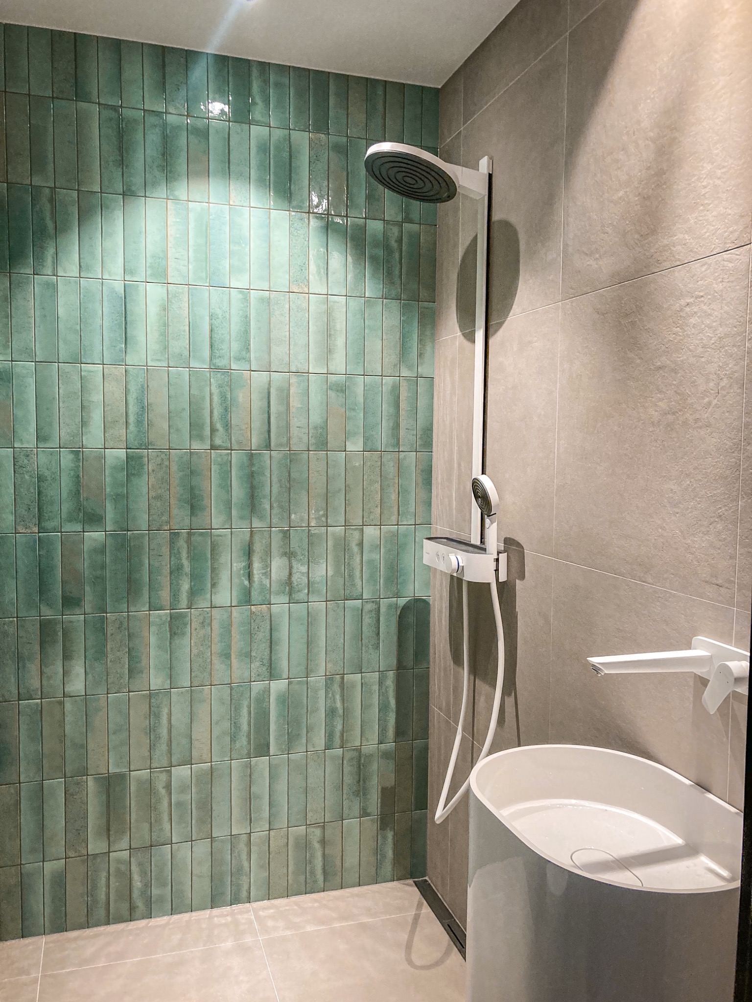 Nowoczesna łazienka z turkusowymi, pionowo ułożonymi płytkami na ścianie prysznicowej, minimalistyczną białą armaturą i szarą płytką podłogową.