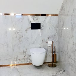 GRESLUX KRZYSZTOF PŁOCINIK - Nowoczesna toaleta podwieszana w łazience wykończonej płytkami imitującymi marmur, z akcentami w kolorze miedzianego złota. Minimalistyczny design.