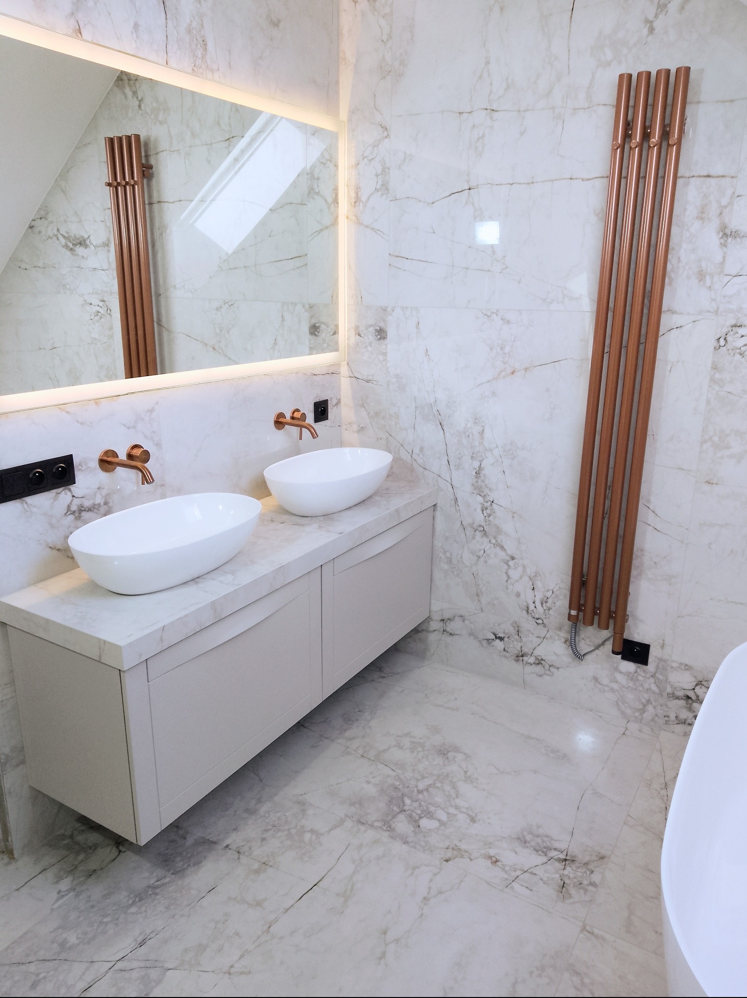 Elegancka łazienka w marmurze z dwoma umywalkami nablatowymi, miedzianą armaturą i grzejnikiem drabinkowym. Lustro z podświetleniem LED.