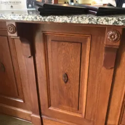 Drewniana lada barowa z dekoracyjnymi elementami rzeźbionymi i blatem z imitacji kamienia, na kt&oacute;rej leżą menu restauracyjne w sk&oacute;rzanych okładkach.