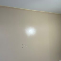 And&Pat Bud - Świeżo pomalowana ściana w odcieniach beżu, z widoczną taśmą malarską przy suficie i wystającymi przewodami elektrycznymi, gotowa do dalszych prac wykończeniowych.