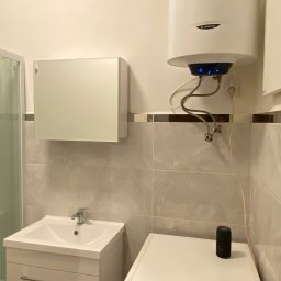 And&Pat Bud - Biała łazienka z umywalką w szafce, pralką Gorenje i wiszącym bojlerem Ariston z podświetleniem LED, płytki w odcieniach beżu.