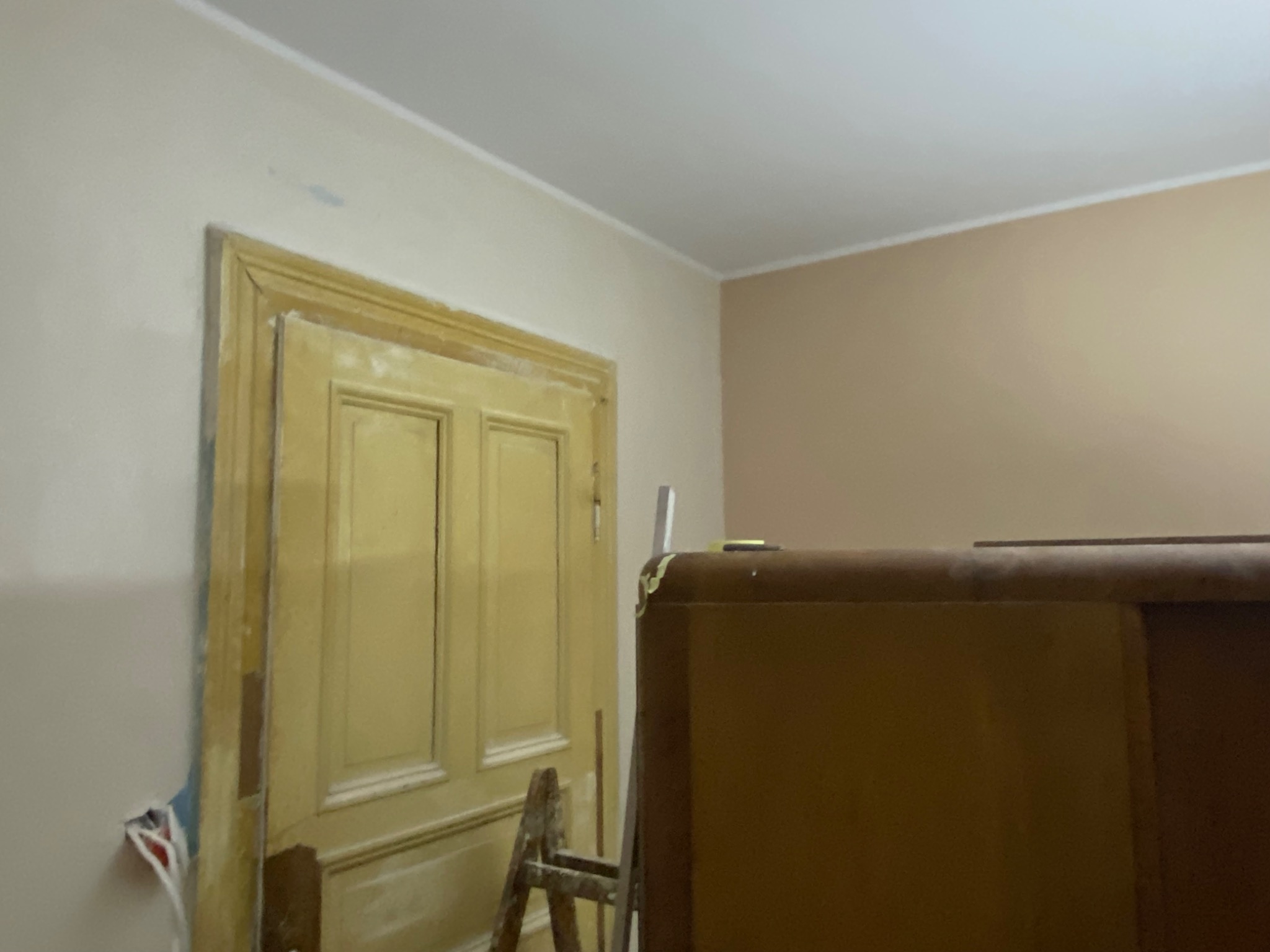 Przygotowania do malowania ścian we Wrocławiu: widoczna stara, drewniana ościeżnica drzwiowa, częściowo oszlifowana i przygotowana do malowania, fragment ściany z widocznymi kablami elektrycznymi...