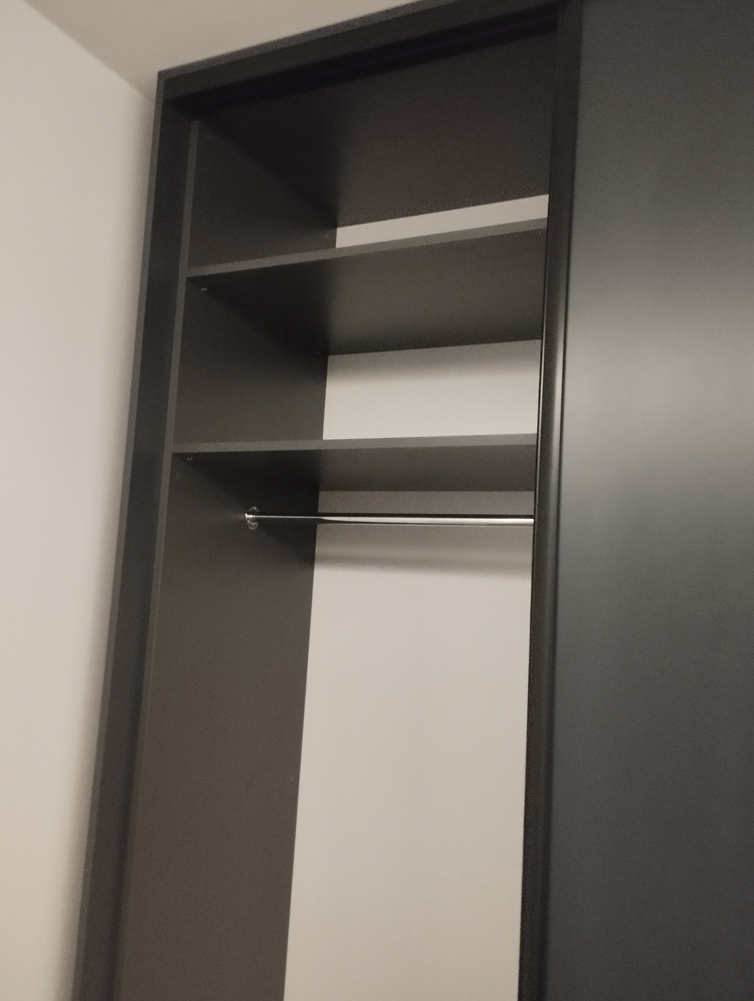 Wnętrze szafy wnękowej z przesuwanymi drzwiami w odcieniach szarości, widoczne półki i metalowy drążek na ubrania, minimalistyczny design.