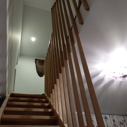 RT-Styl - Drewniane schody z ażurową balustradą z pionowych listew, widok z dołu. Na ścianie drewniany zegar. W tle zasłony w motyle.