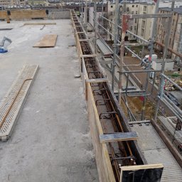 Sasza Korniychuk - Szczecin: Zbrojenie w szalunku na dachu budynku w trakcie budowy, widoczne rusztowania i panorama miasta w tle.
