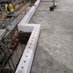 Sasza Korniychuk - Wznoszone ściany z betonu komórkowego na budowie, widoczne rusztowania, zwijarka kabli i narzędzia w wiadrach na szarej betonowej powierzchni.