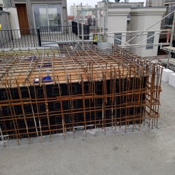 Sasza Korniychuk - Zbrojenie szalunku fundamentu na dachu budynku wielorodzinnego, widoczne elementy konstrukcji i rusztowania w tle.