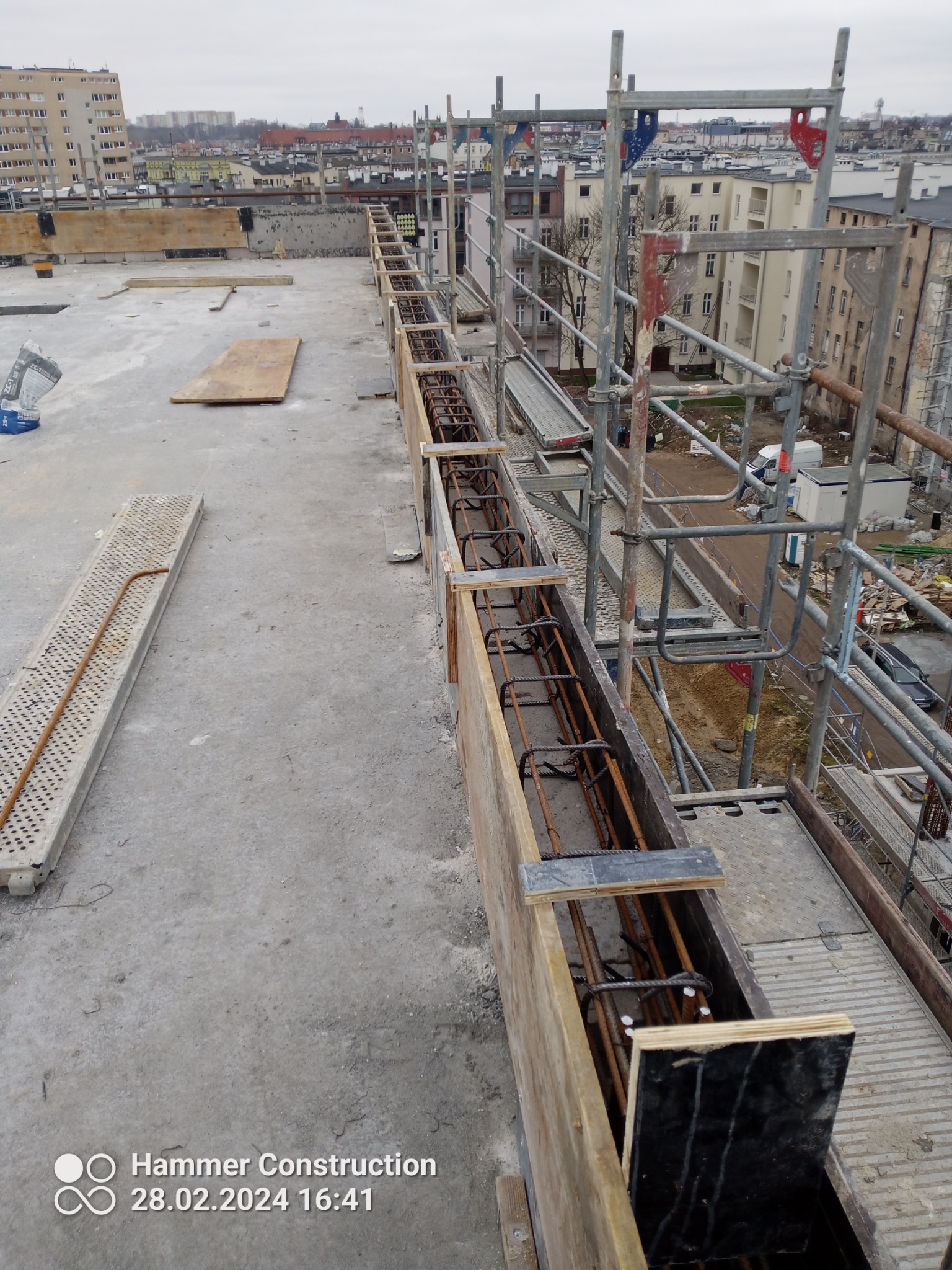 Szczecin: Zbrojenie w szalunku na dachu budynku w trakcie budowy, widoczne rusztowania i panorama miasta w tle.