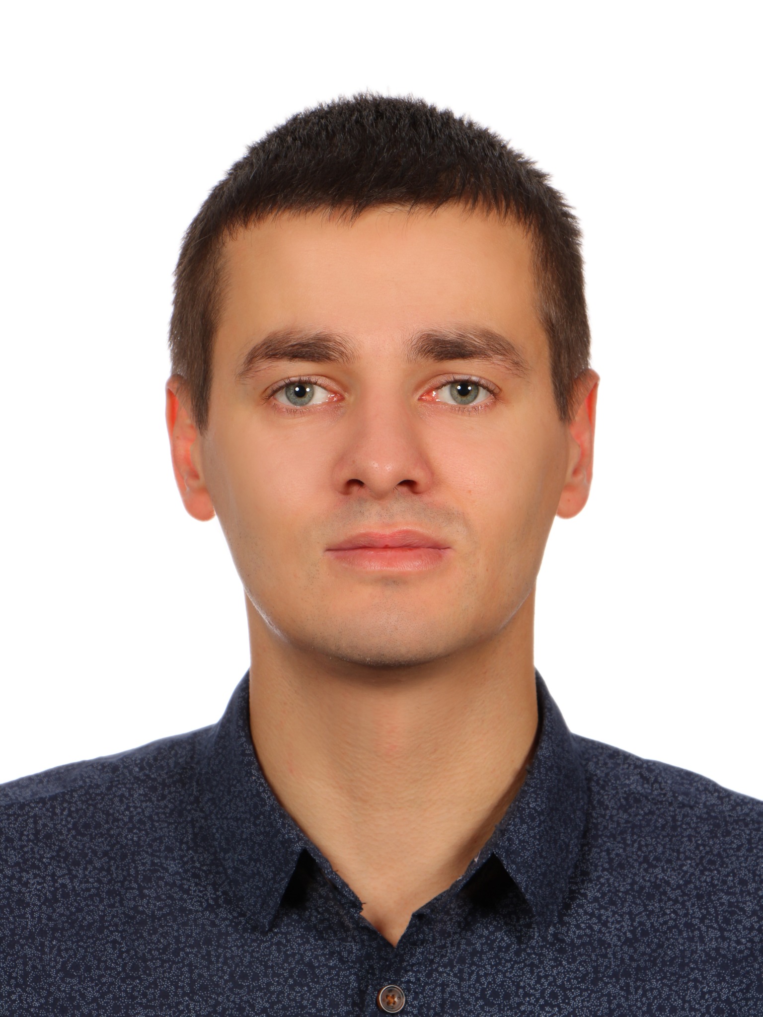 Portret młodego mężczyzny z krótkimi ciemnymi włosami i niebieską koszulą z drobnym wzorem na białym tle.