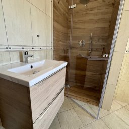 Rubicon - Nowoczesna łazienka z drewnopodobnymi płytkami w kabinie prysznicowej typu walk-in i szafką pod umywalką z dwiema szufladami o fakturze jasnego drewna.