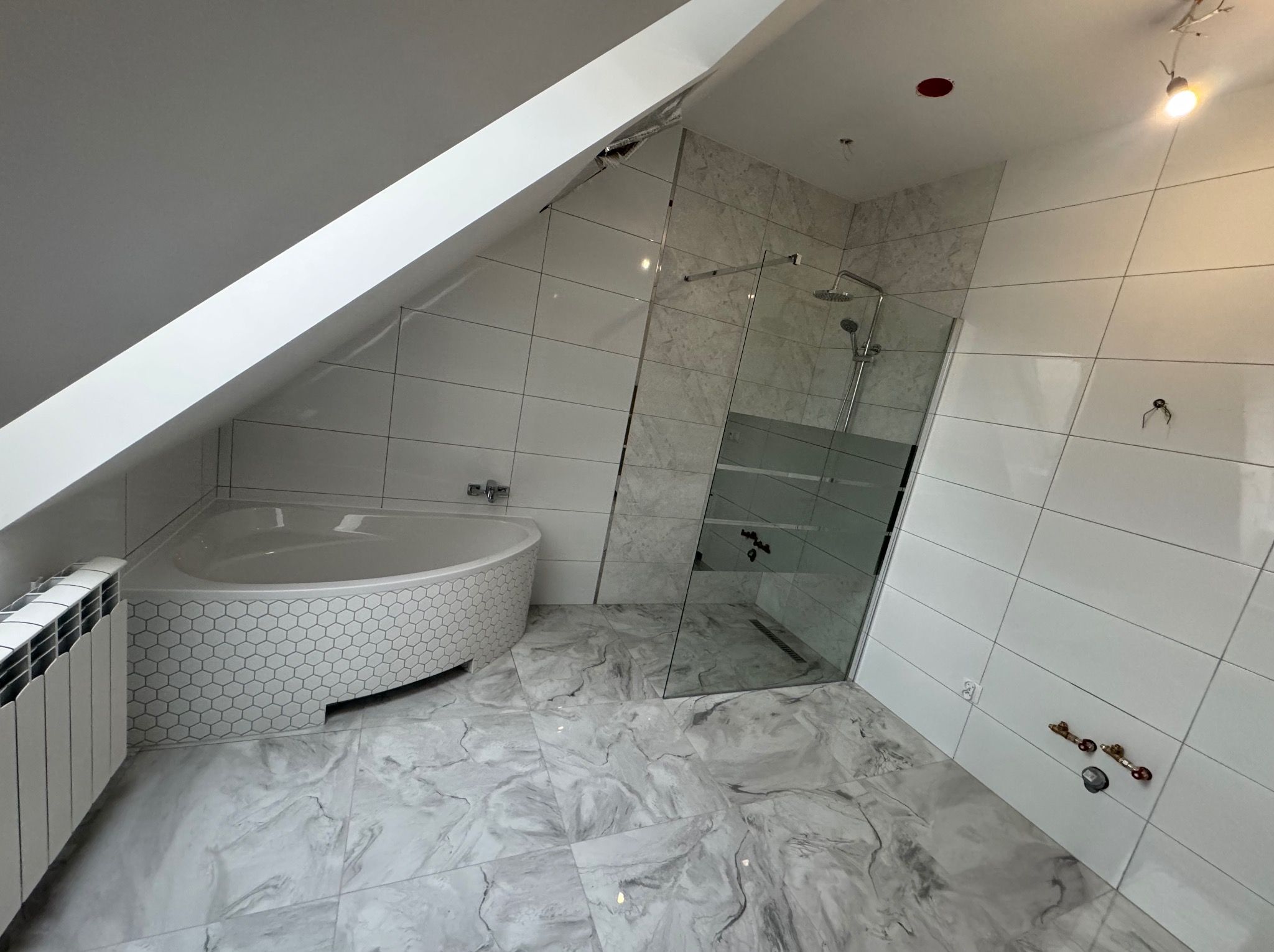 Nowoczesna łazienka na poddaszu z narożną wanną obłożoną heksagonalnymi płytkami, kabiną prysznicową typu walk-in i marmurową podłogą w odcieniach szarości i bieli.