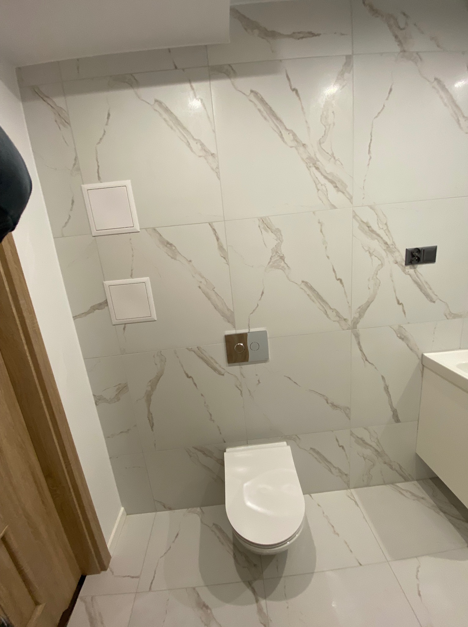 Nowoczesna łazienka z białymi płytkami imitującymi marmur, podwieszana toaleta i ukryte rewizje inspekcyjne.