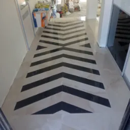 Ułożona podłoga z płytek w jodełkę w odcieniach beżu i czerni, widoczny fragment pomieszczenia w trakcie wykańczania, narzędzia i materiały budowlane w tle.