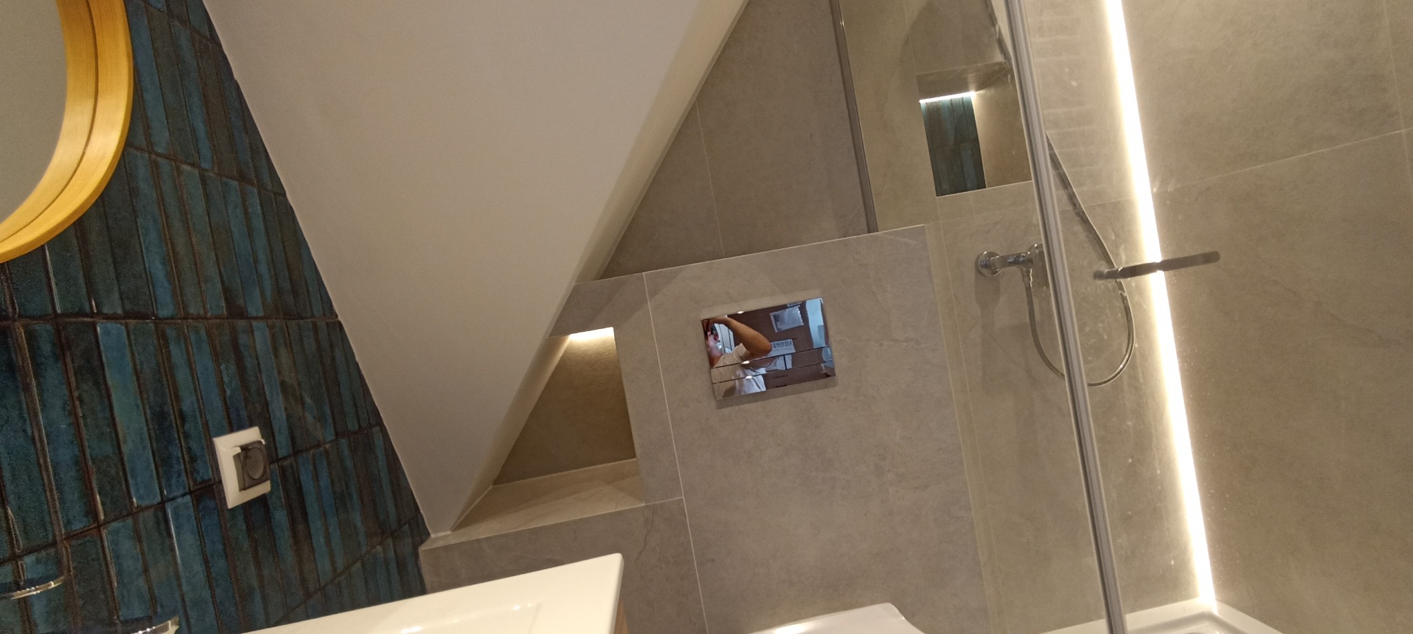 Wykończona łazienka z niebieską mozaiką, okrągłym lustrem, oświetloną wnęką i kabiną prysznicową ze szklanymi drzwiami. Nowoczesny design.