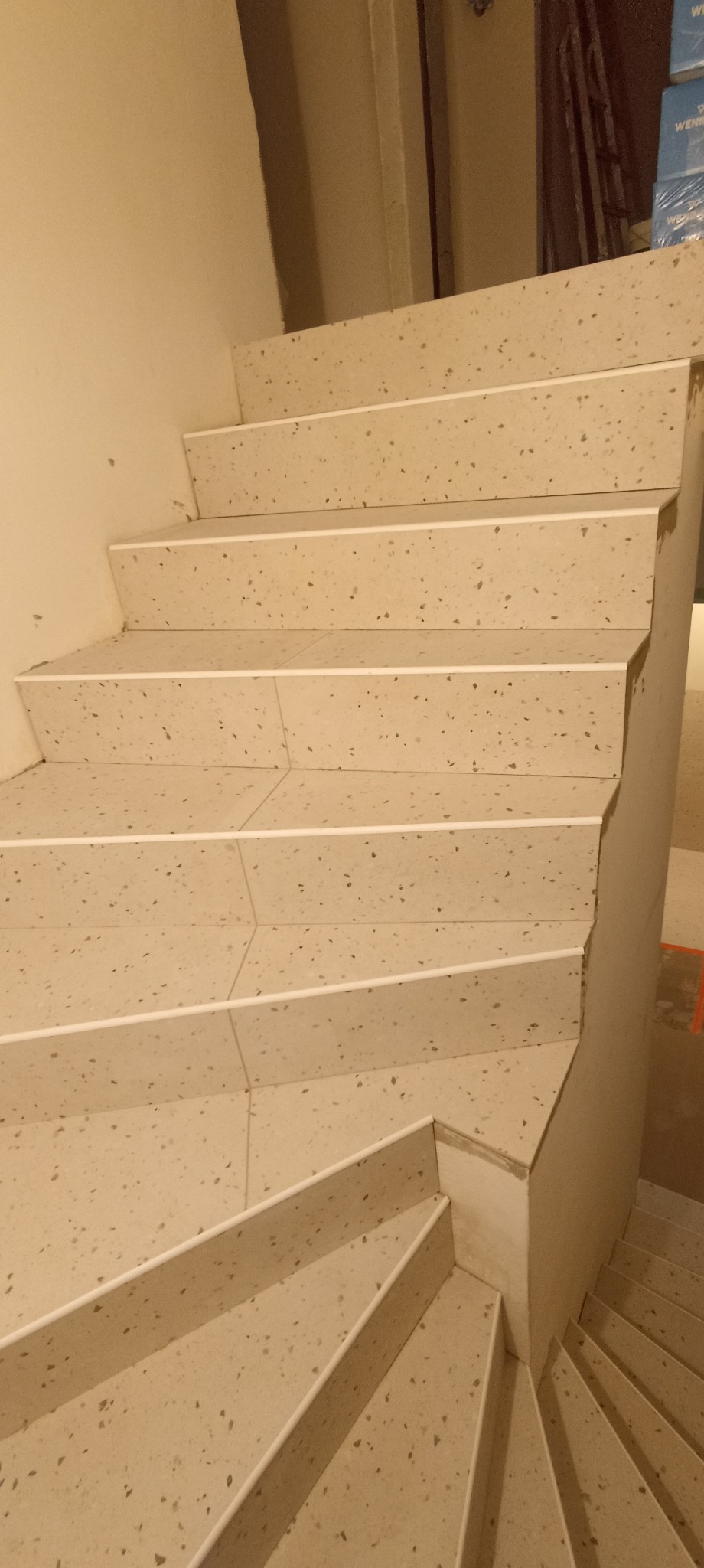 Wykończone schody z płytek imitujących lastryko, z białymi listwami wykończeniowymi. Widok z dołu, schody skręcają w prawo.