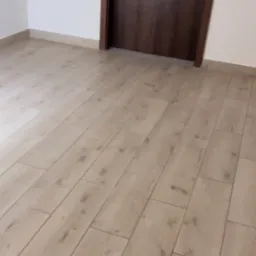 Ukończone podłogi z paneli imitujących drewno w jasnym kolorze, widok na brązowe drzwi i białe ściany.