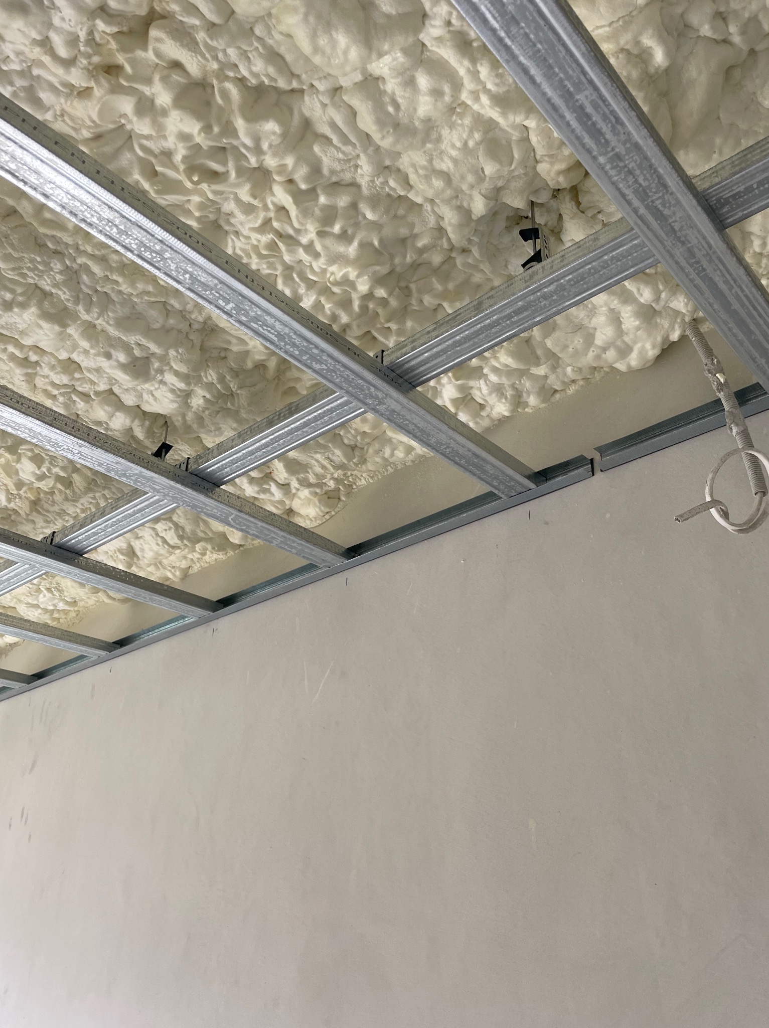 Konstrukcja metalowa sufitu podwieszanego wypełniona pianą montażową, widoczne przewody elektryczne, ściana w tle przygotowana pod gładzie.