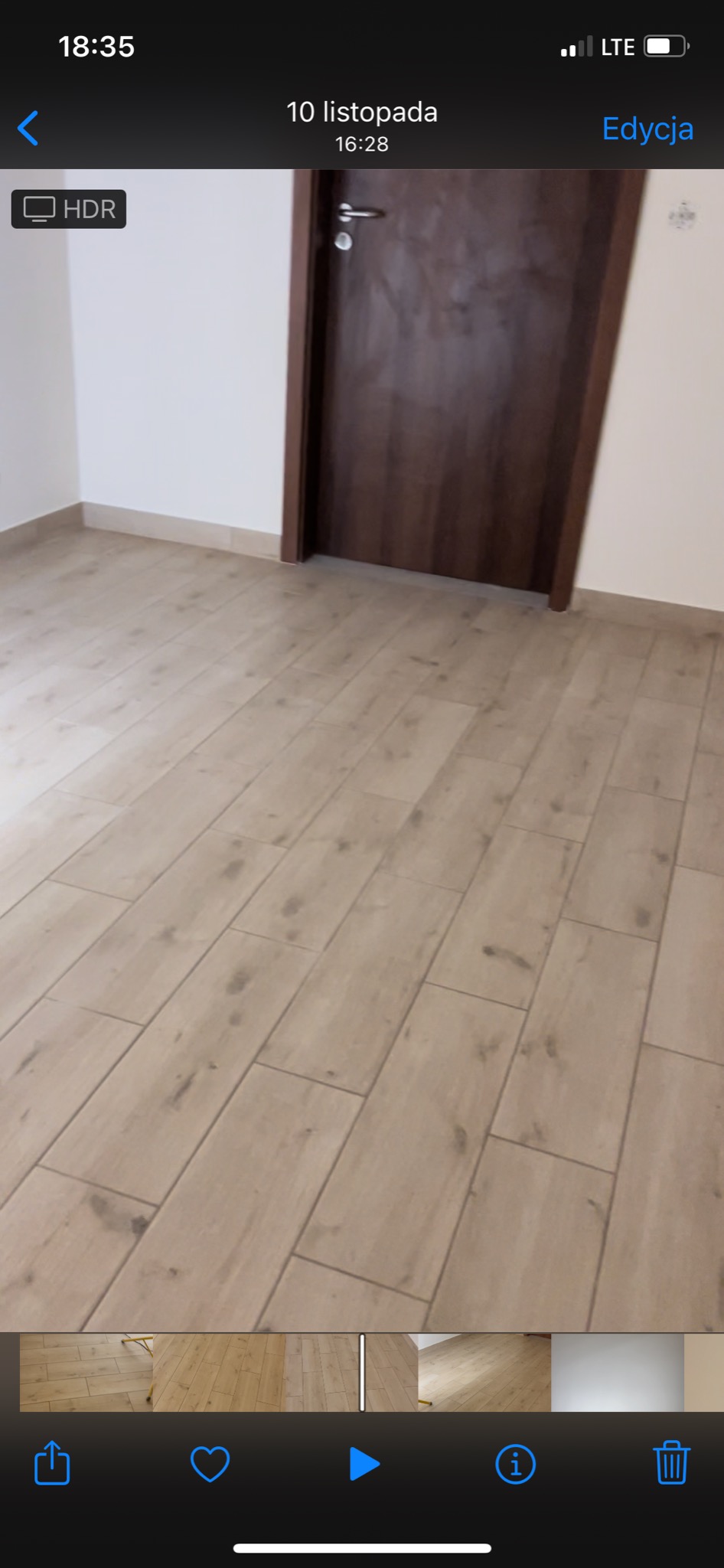 Ukończone podłogi z paneli imitujących drewno w jasnym kolorze, widok na brązowe drzwi i białe ściany.