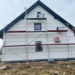 Elewacje budynków - Dom jednorodzinny w trakcie prac elewacyjnych, widoczne rusztowanie, paczka materiału izolacyjnego Swissopor Lambda i zabezpieczone okna folią.