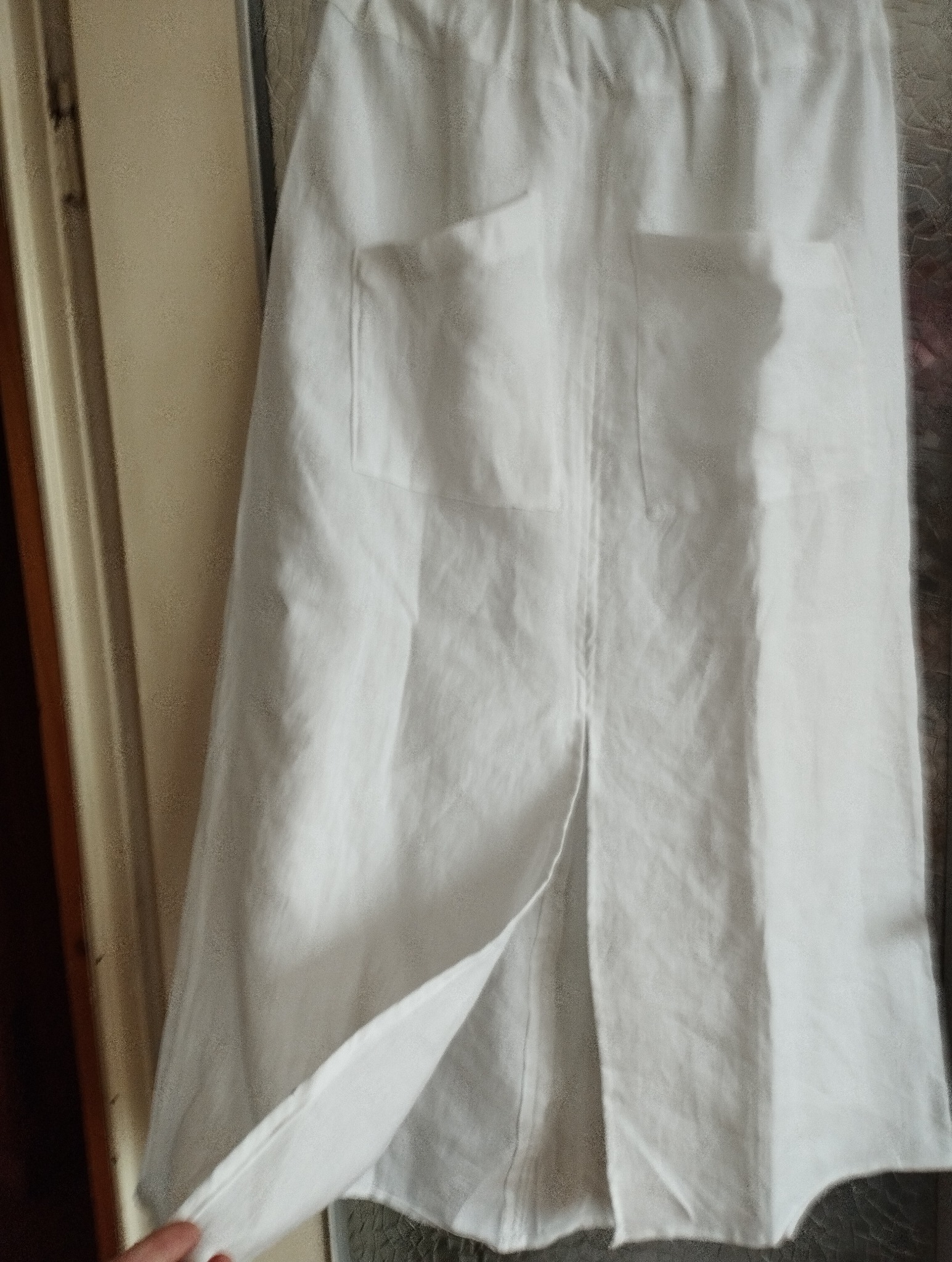 Lniania biała spódnica z kieszeniami i rozcięciem z przodu, wisząca na drzwiach.