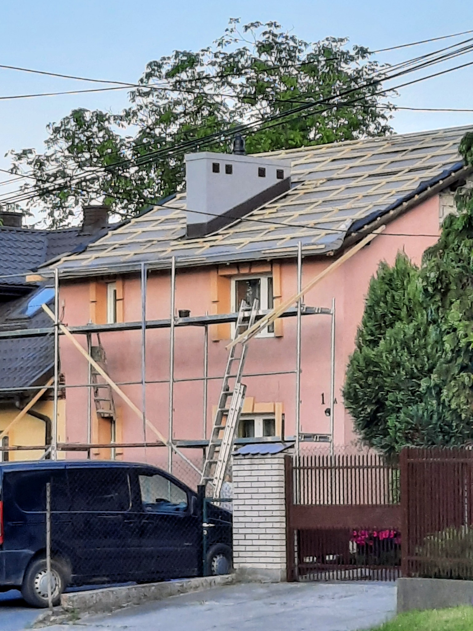 Dom w trakcie renowacji dachu, widoczne rusztowania, przygotowana konstrukcja pod pokrycie, komin z szarej blachy.