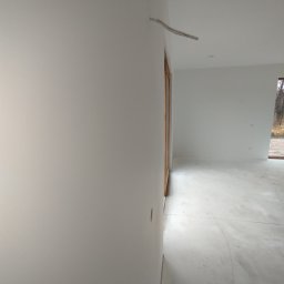 F.T.D.J Fachowa termomodernizacja domków jednorodzinnych Tomasz Jabłoński - Białe, świeżo pomalowane ściany wewnętrzne z wystającymi kablami w nowym domu. Widoczna stolarka okienna i drzwiowa z naturalnego drewna. Minimalistyczny styl.