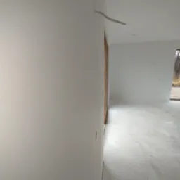 Białe, świeżo pomalowane ściany wewnętrzne z wystającymi kablami w nowym domu. Widoczna stolarka okienna i drzwiowa z naturalnego drewna. Minimalistyczny styl.