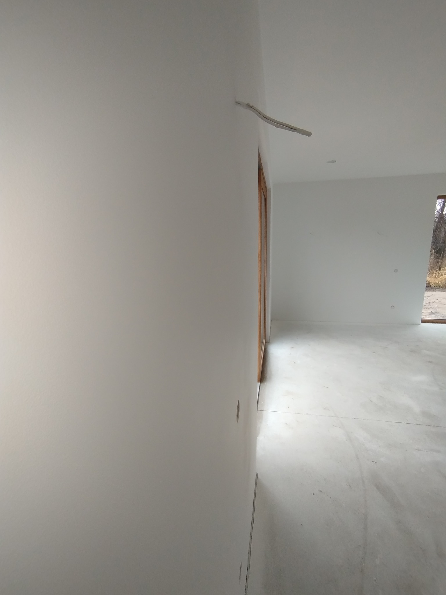 Białe, świeżo pomalowane ściany wewnętrzne z wystającymi kablami w nowym domu. Widoczna stolarka okienna i drzwiowa z naturalnego drewna. Minimalistyczny styl.