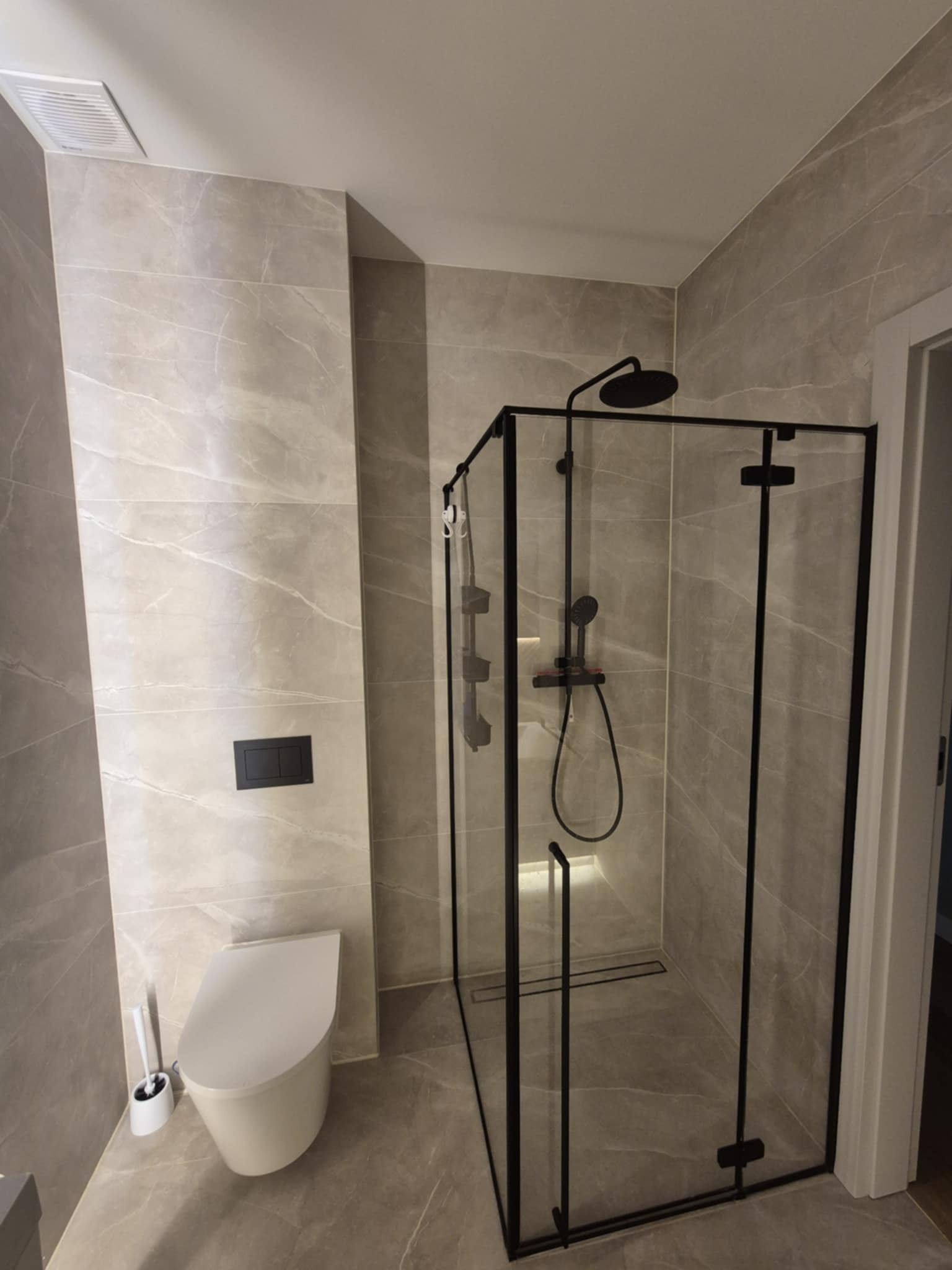 Nowoczesna łazienka z kabiną prysznicową typu walk-in z czarnymi profilami, podwieszaną toaletą i płytkami imitującymi marmur. Minimalistyczny design.