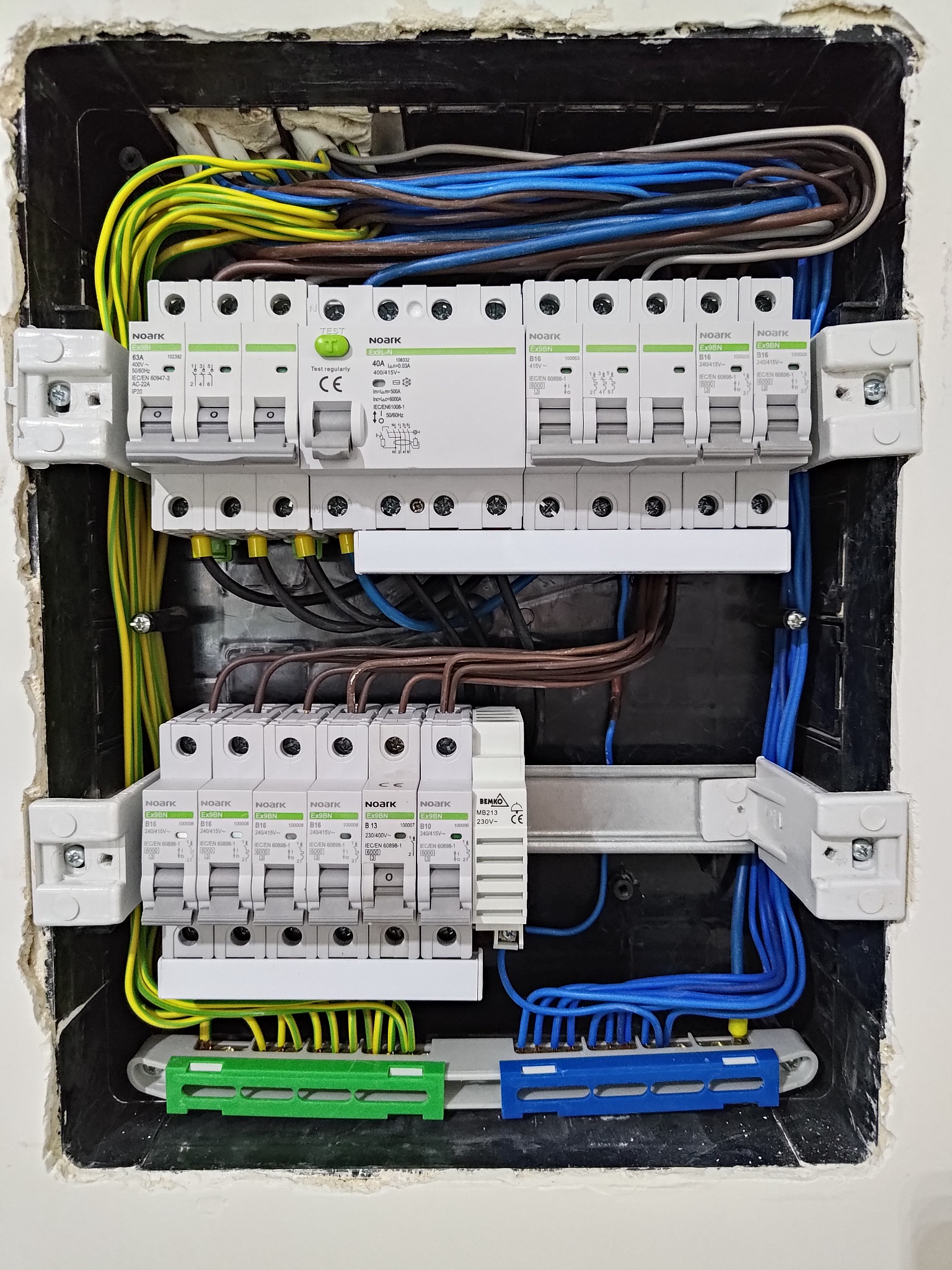 Rozdzielnica elektryczna z zainstalowanymi bezpiecznikami i okablowaniem w ścianie w Krakowie, widoczne przewody w kolorach niebieskim, żółto-zielonym i brązowym.