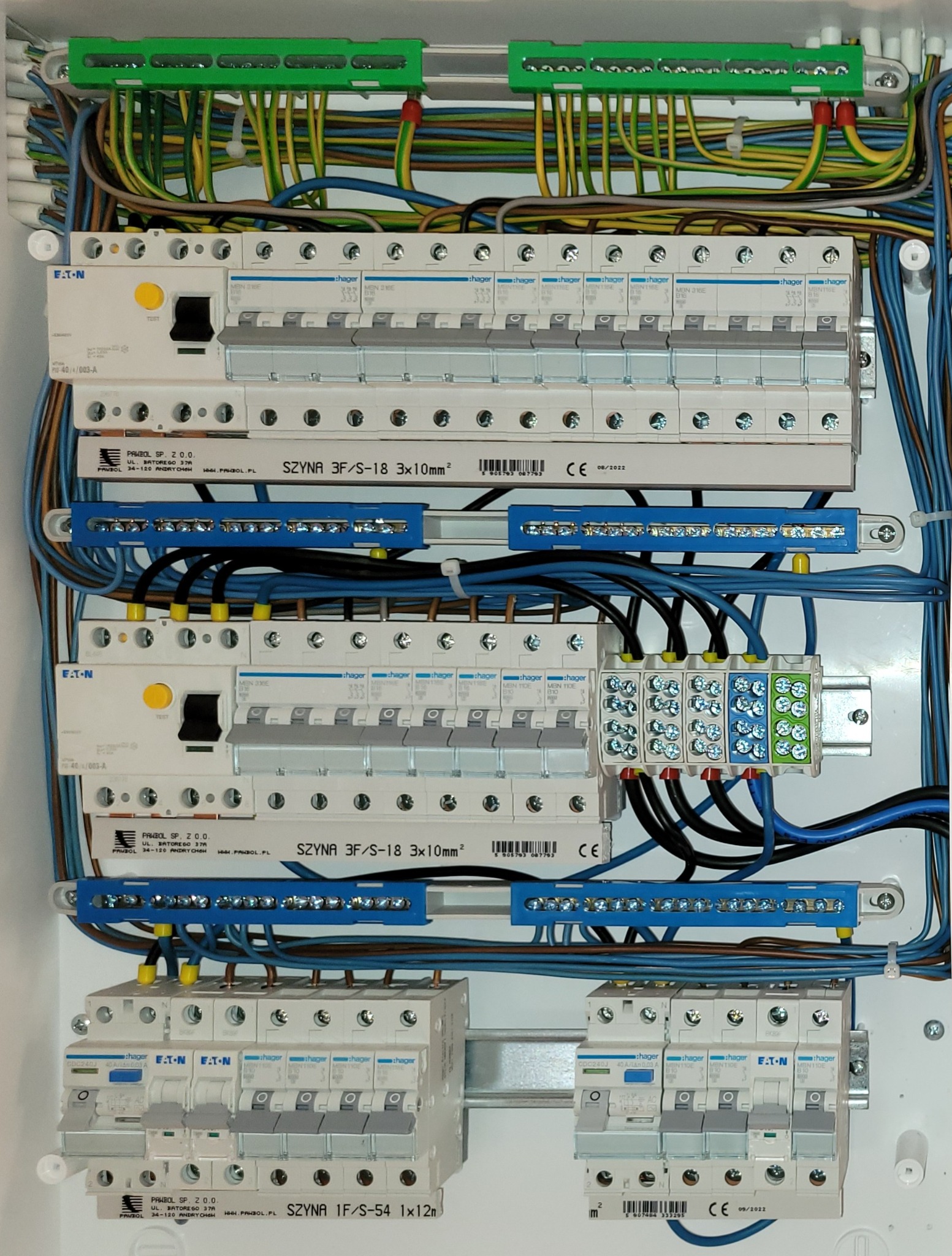 Rozdzielnica elektryczna z zabezpieczeniami różnicowoprądowymi i nadprądowymi firm Hager i Eaton, okablowana przewodami w kolorach żółto-zielonym, niebieskim i czarnym, z szynami zbiorczymi...