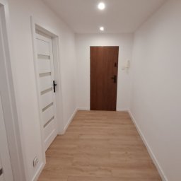 VITALII DERDIIENKO VIDE-REM - Jasny korytarz po remoncie: białe ściany, panele podłogowe w odcieniach drewna, dwoje drzwi. Minimalistyczny design, czyste linie, nowoczesne oświetlenie.